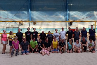 Gruppenfoto der Beachvolleyball-Spieler*innen auf dem Sandplatz