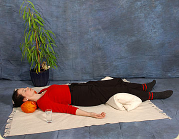 Eine Person liegt entspannt auf einer Decke am Fußboden.