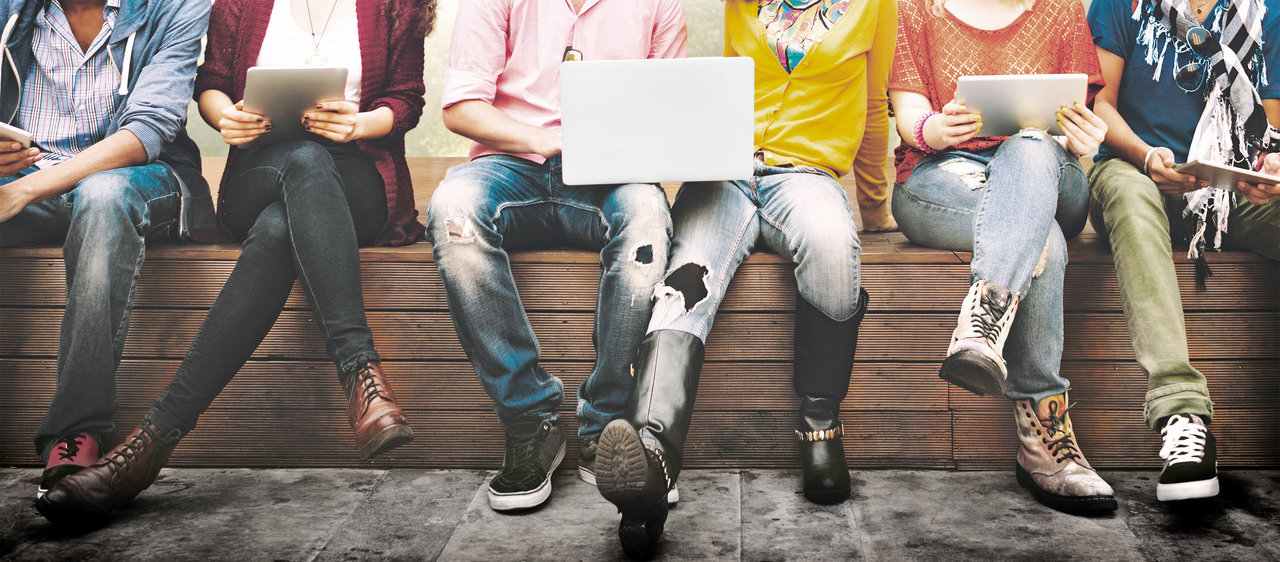 Studierende sitzen mit Laptops und Tablets auf einer Bank 