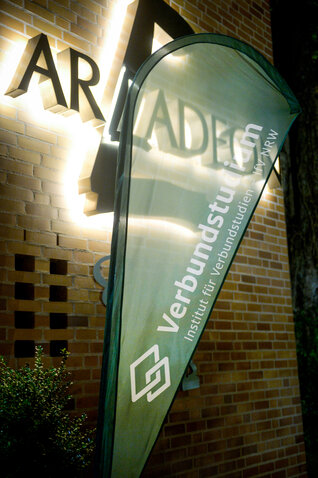 Beachflag "Verbundstudium – Institut für Verbundstudien – IfV NRW" vor dem Eingangsbereich des Arcadeon