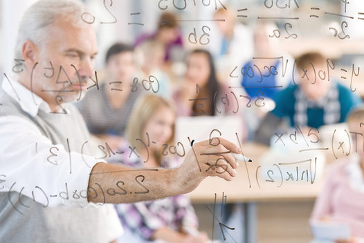 Lehrender schreibt im Präsenzunterricht mathematische Formeln an die Tafel